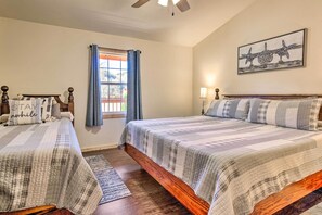A bedroom with two beds, a window with curtains, a ceiling fan, and a wall-mounted artwork.