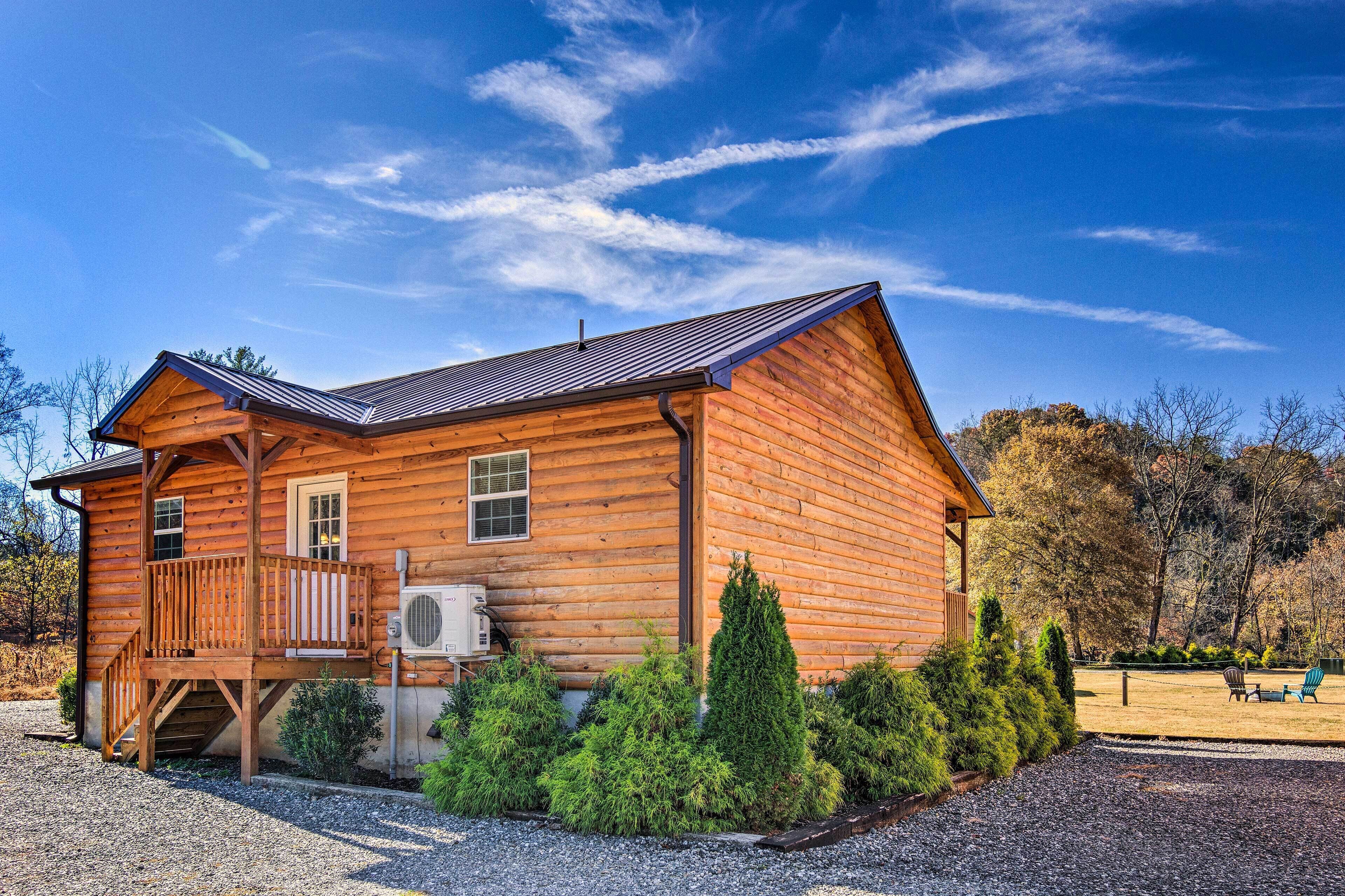 A wooden cabin with a balcony, a covered porch, and a gravel driveway.
