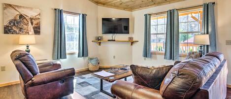A living room with leather sofas, a flat-screen TV, and a wooden ceiling.