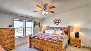 A bedroom with a wooden bed, a ceiling fan, two bedside tables with lamps, a dresser, and a window with a view. - Desert Escape Off I-10 w/ Over 1 Enclosed Acre! (Benson)
