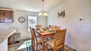 A dining area with a wooden table set for four, surrounded by chairs with cushioned seats. A chandelier hangs from the ceiling, and a decorative wall piece of horses is visible. - Desert Escape Off I-10 w/ Over 1 Enclosed Acre! (Benson)