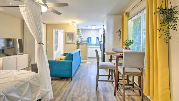 A modern living room with a TV, a blue sofa, a dining table with chairs, and a ceiling fan. - 2 Mi to Asu: Studio w/ Private Hot Tub in Tempe (Tempe)