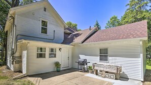 A two-story house with a covered patio area, a grill, and a small wooden bench.