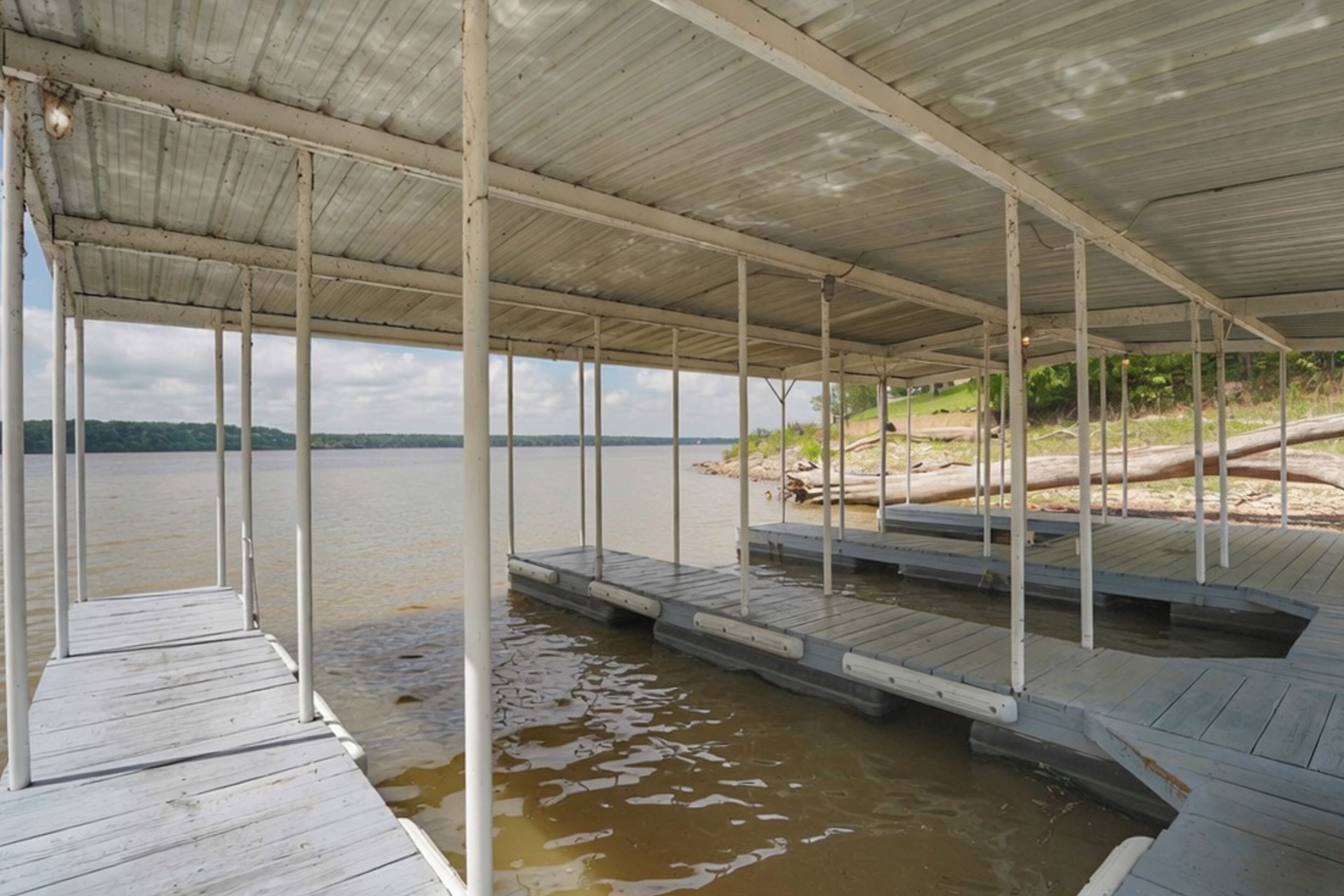 A covered dock extending into a body of water with a metal roof and wooden planks.