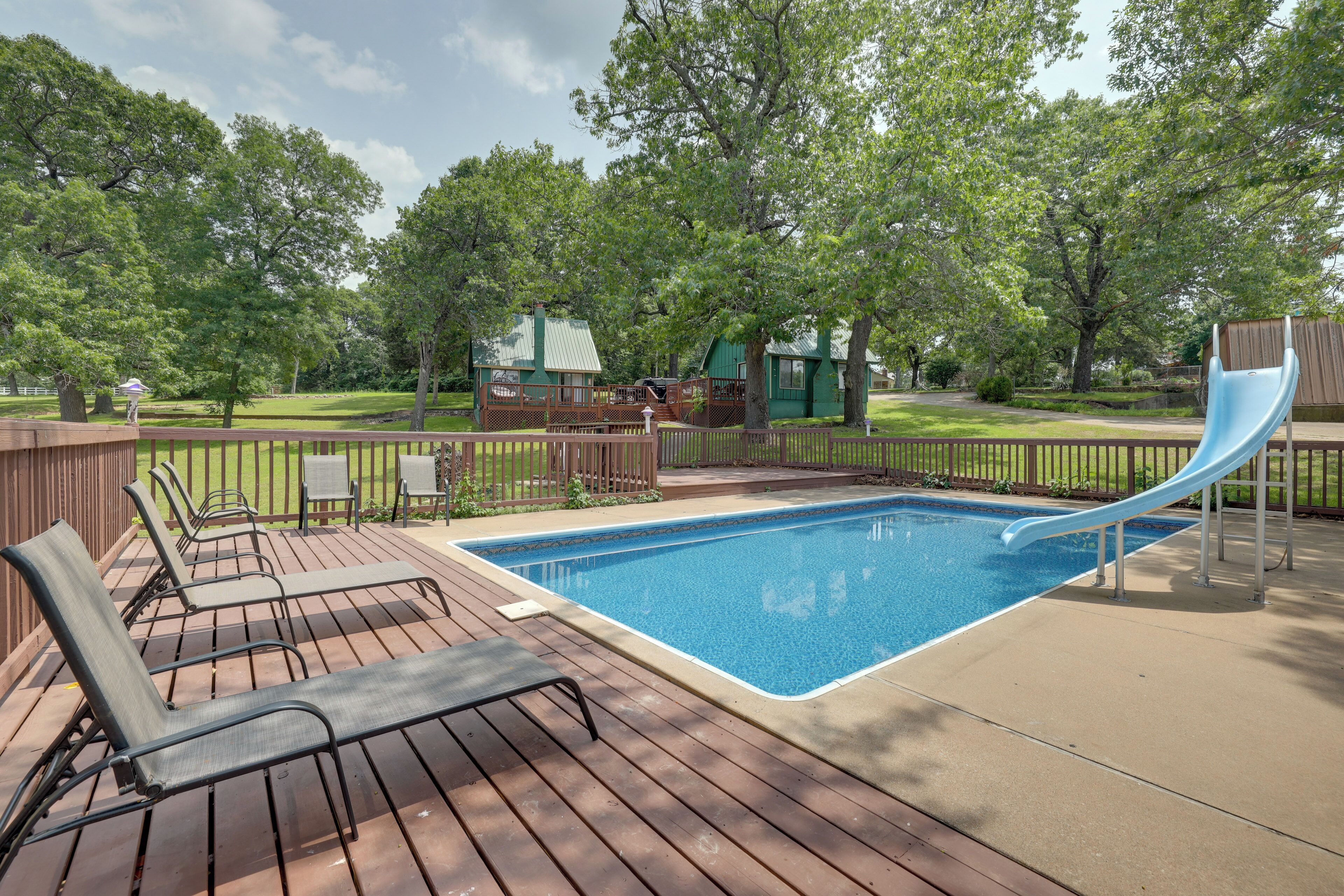 A backyard with a swimming pool, a slide, and a deck with lounge chairs.
