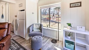 A modern living room with a brown leather sofa, a grey armchair, and a round ottoman. A white bookshelf with a 'wifi' sign is visible, and a 'CABIN' sign hangs on the wall. - Lakefront Cabin: Boat Dock, Pool & Hot Tub (Grove)