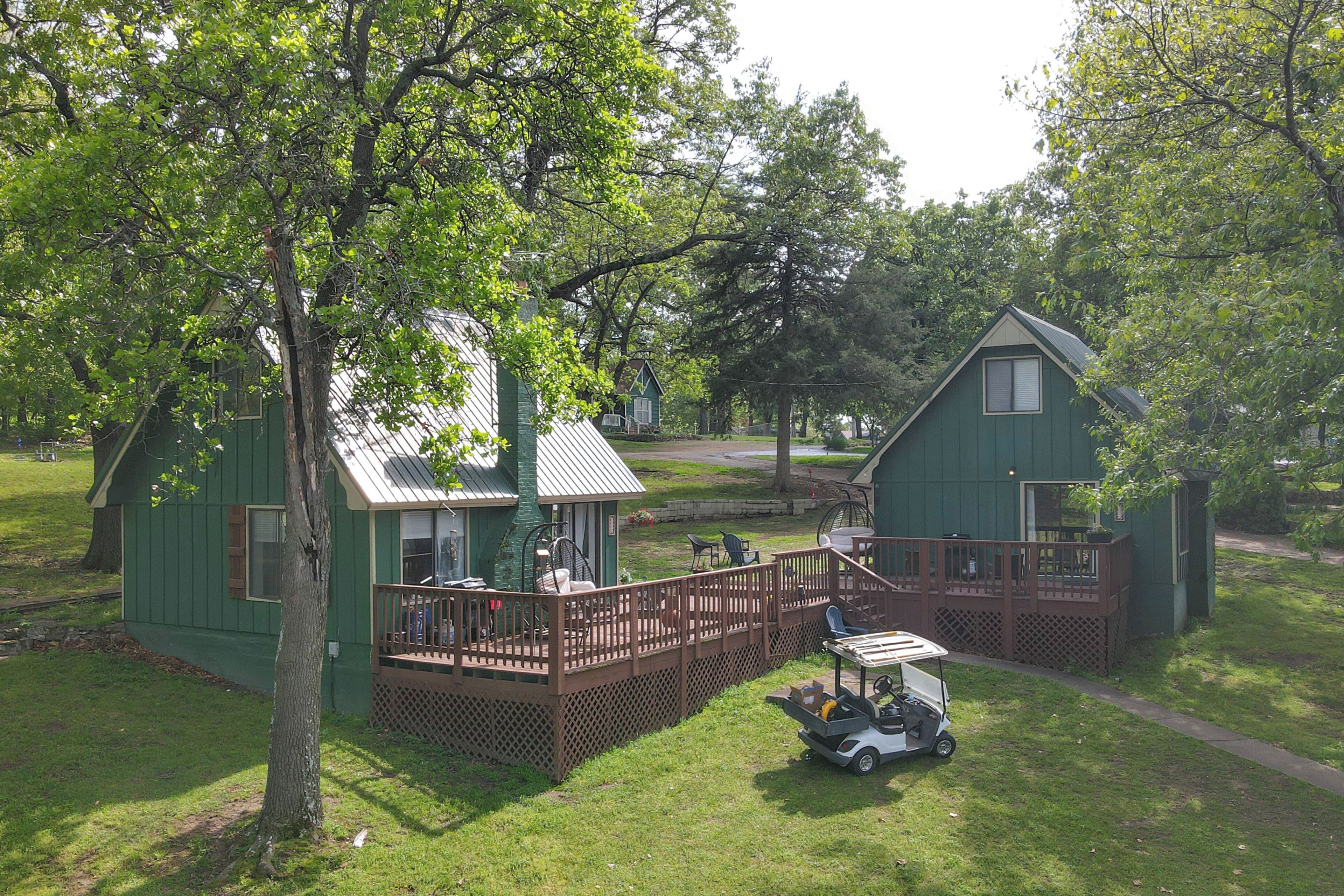 Une cabane verte avec une terrasse, un véhicule de golf et un grand arbre au premier plan.