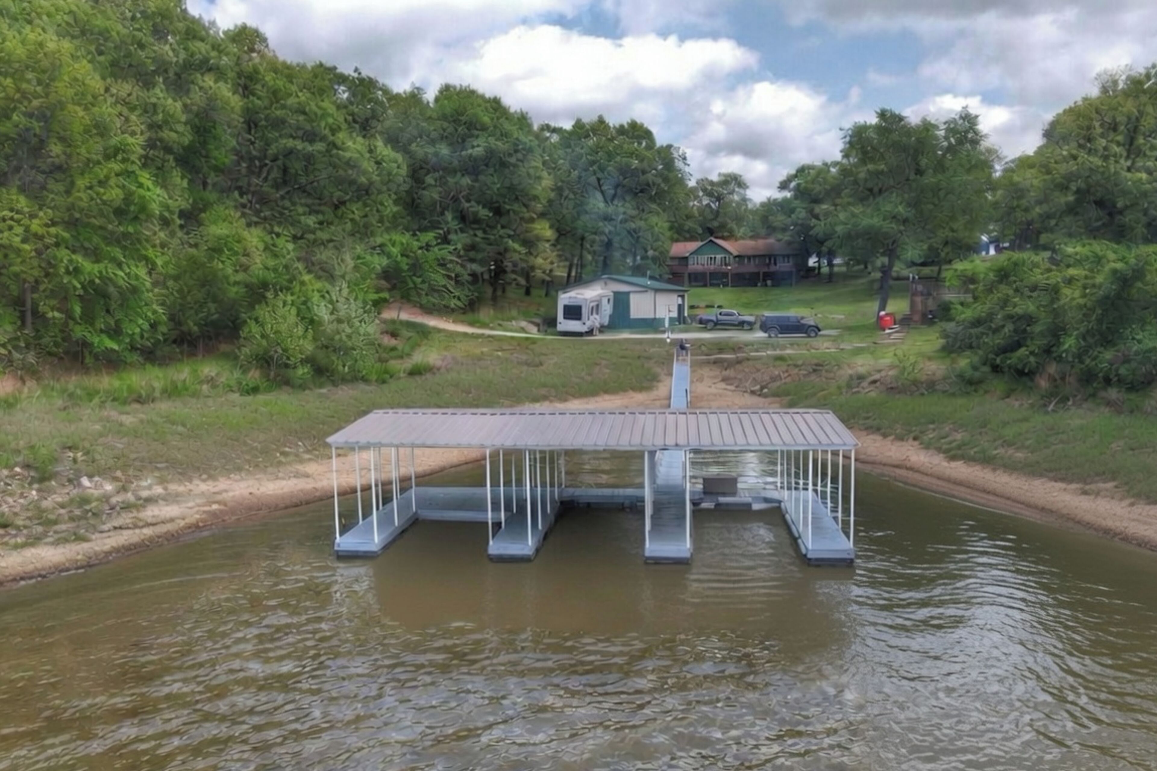 A dock with a covered walkway over water, surrounded by greenery and a house in the background.