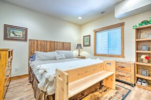 A bedroom with a wooden bed, a nightstand, a lamp, a window with blinds, and a shelf with decorative items. - Ronald Home w/ Direct Cle Elum Lake Access! (Cle Elum)