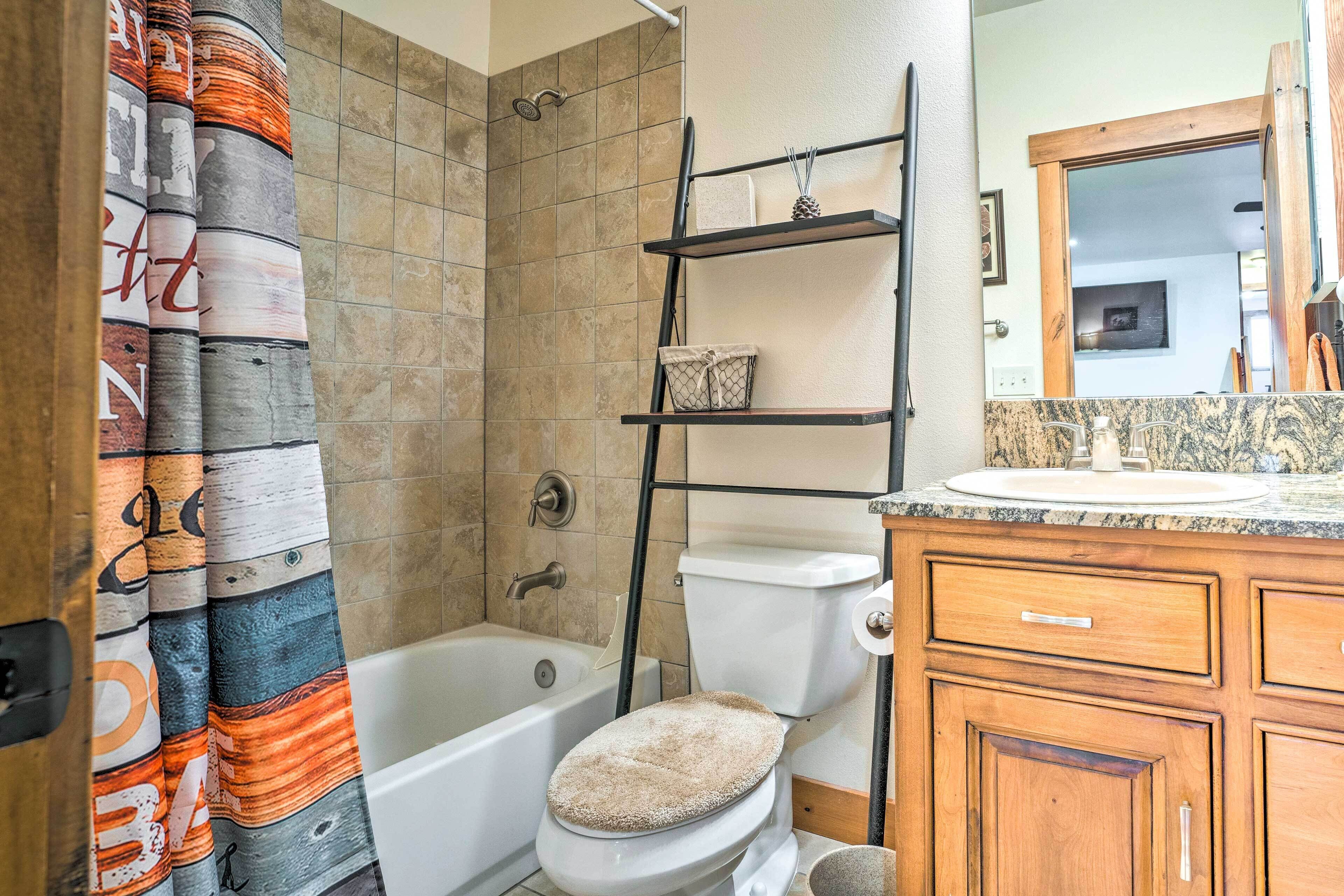 A bathroom with a bathtub, toilet, and a shower area. There is a towel rack above the toilet and a shelf with a decorative item.