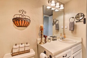 Casa de banho com sanita, lavatório, espelho e apliques decorativos.