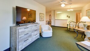 A hotel room with a wooden dresser, a television, a white armchair, a dining table with chairs, and a ceiling fan. - Cozy Pigeon Getaway, Close to Public Beaches! (Pigeon)