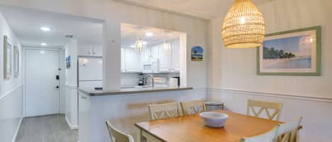 Un comedor con mesa y sillas de madera, una cocina con armarios blancos y una lámpara colgante.