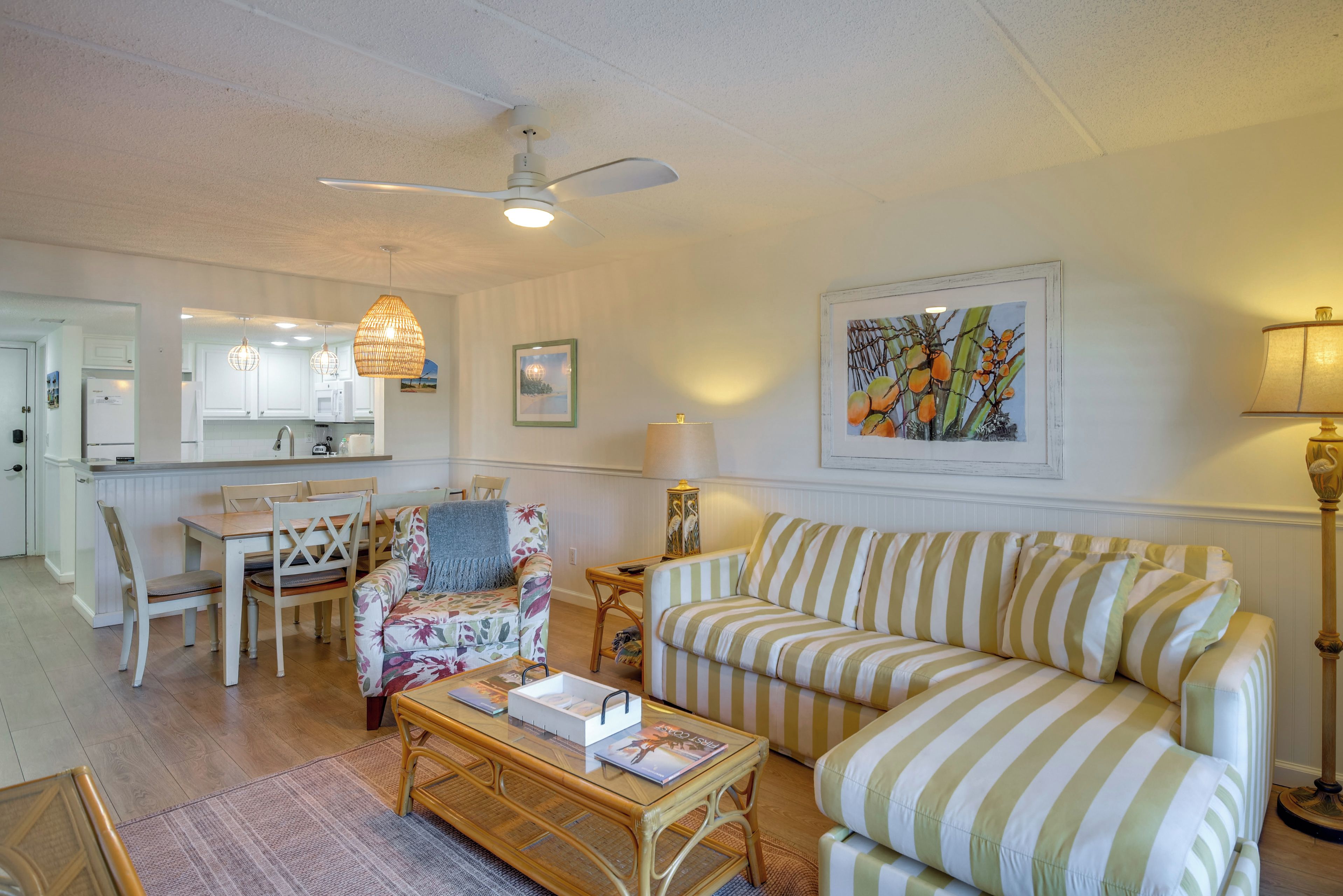 A living room with a striped sofa, a floral armchair, a wooden coffee table, and a dining area with a white table and chairs.