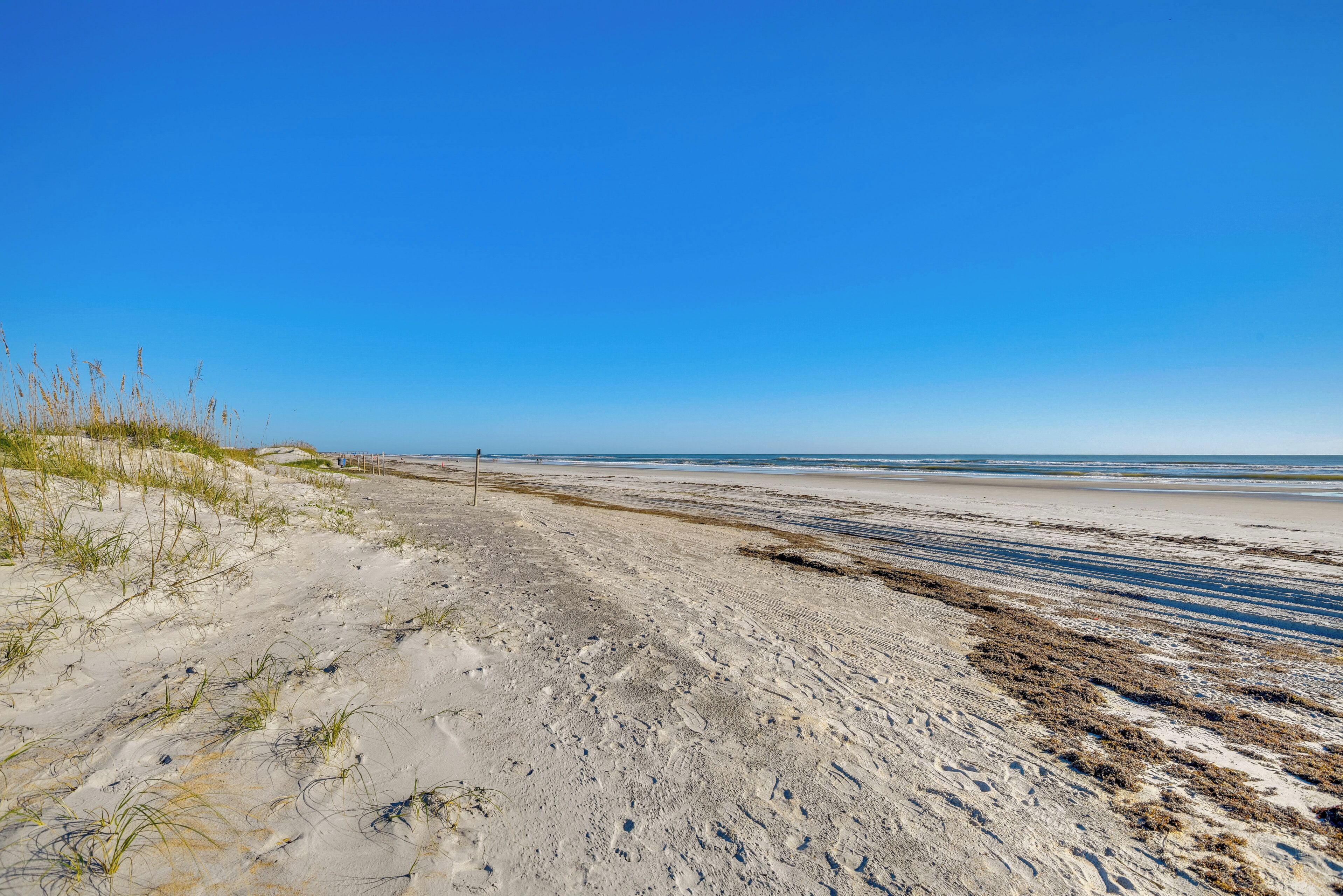 A sandy beach with sparse vegetation and a clear blue sky.