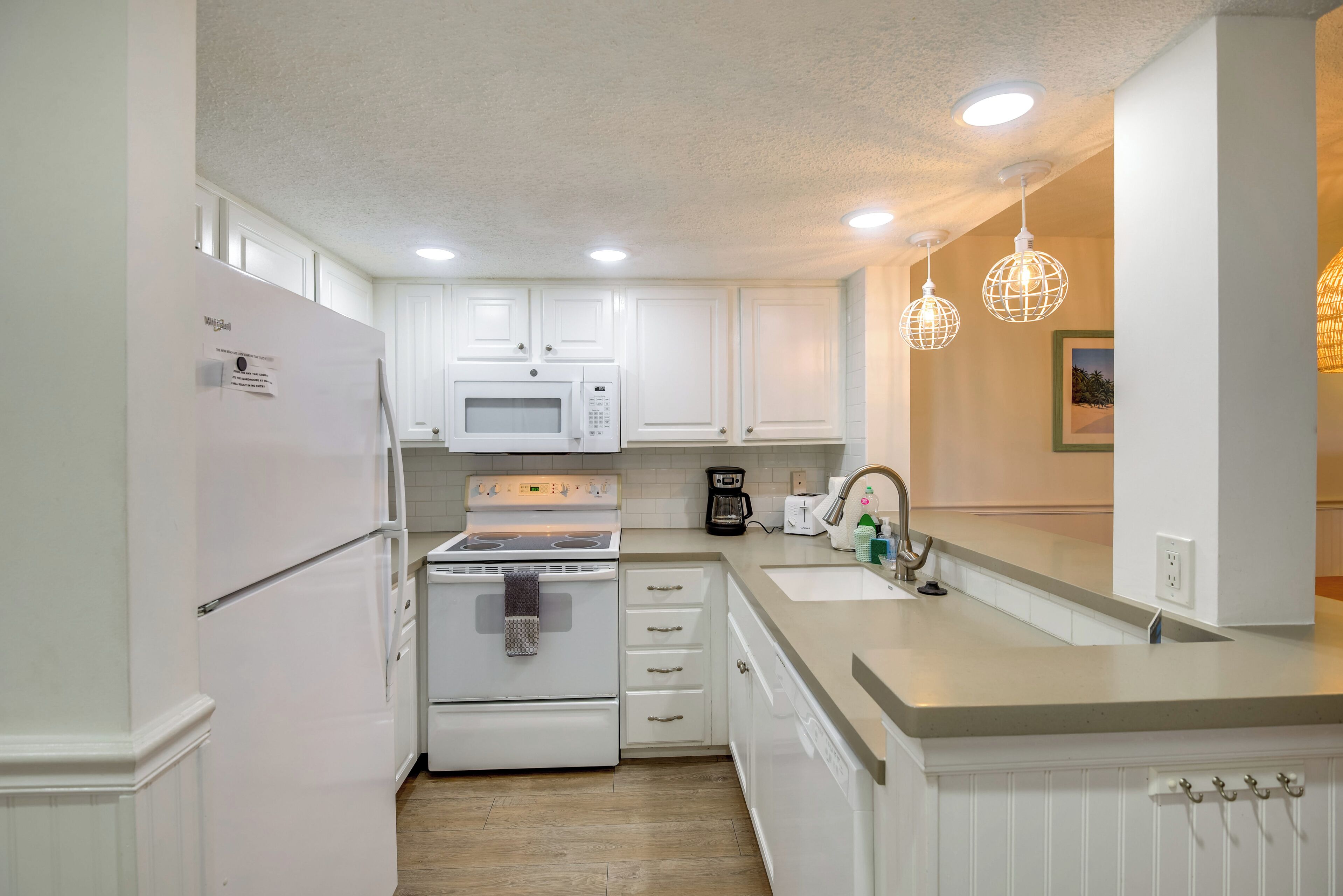 A modern kitchen with white cabinetry, a built-in oven, microwave, and a sink.