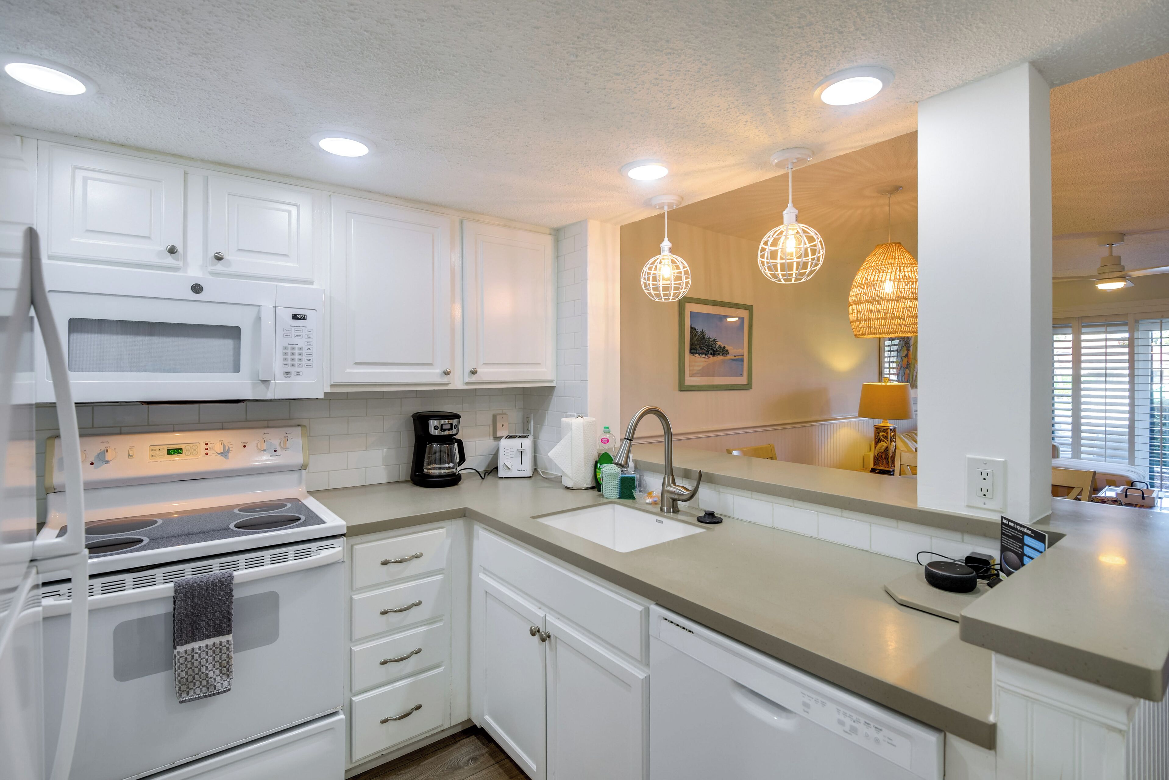 A modern kitchen with white cabinets, a built-in microwave, a stove, and a sink. There are pendant lights and a framed picture on the wall.