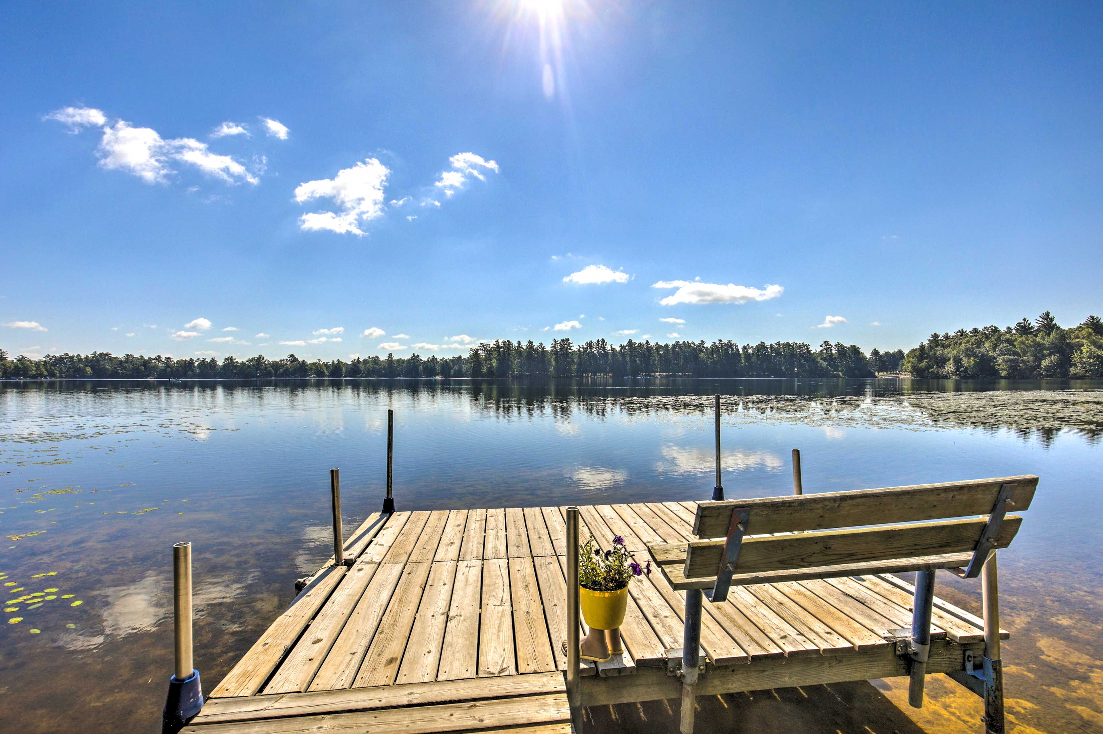 A wooden dock extending into a calm lake with a clear sky and distant trees.