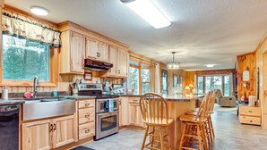 A spacious kitchen with wooden cabinets, a central island with bar stools, and large windows offering a view of the outdoors. - Outdoor Lover's Paradise w/ Dock & Fire Pit! (Woodruff)