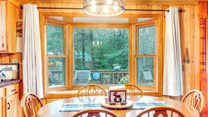 A wooden dining room with a large bay window, wooden chairs, and a table set with a placemat and a decorative item. - Outdoor Lover's Paradise w/ Dock & Fire Pit! (Woodruff)