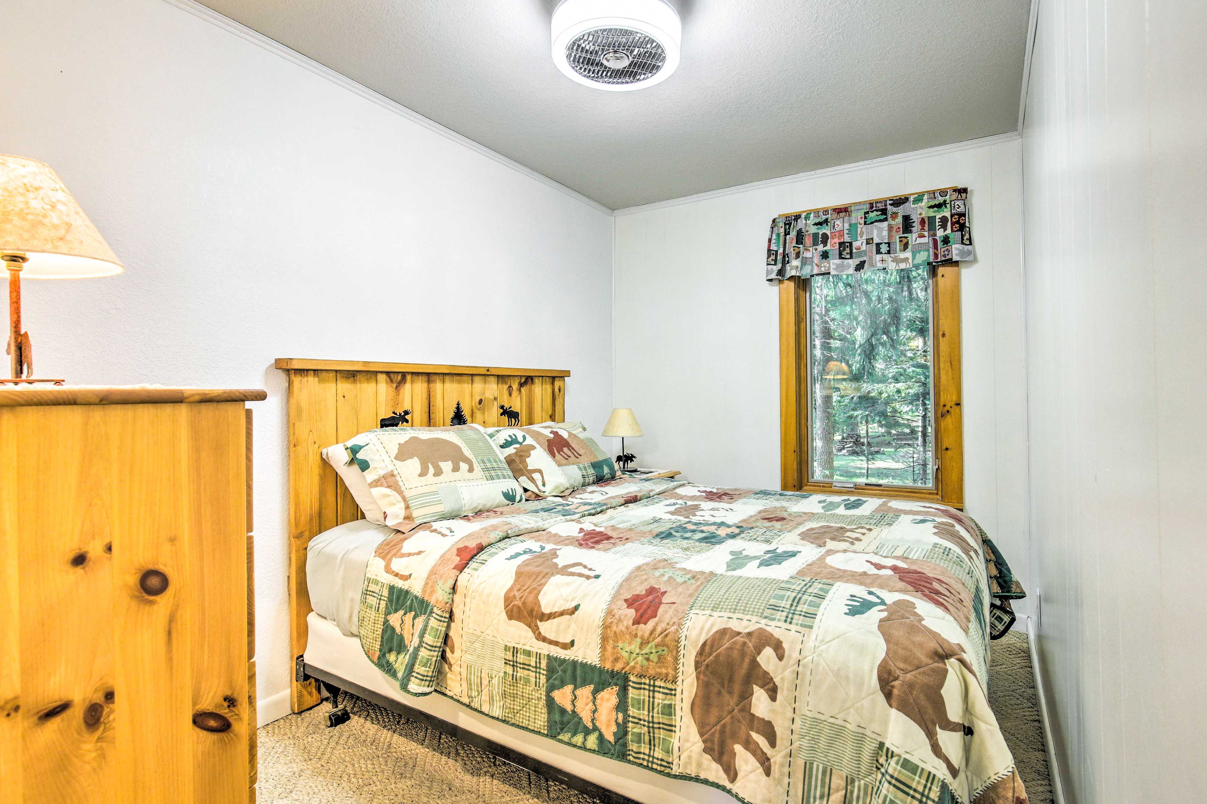 Un dormitorio con cama de madera, ventana con vistas a árboles y lámpara sobre una mesita de noche de madera.