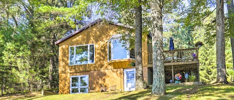 A wooden cabin with two main floors, large windows, and a balcony with outdoor seating.