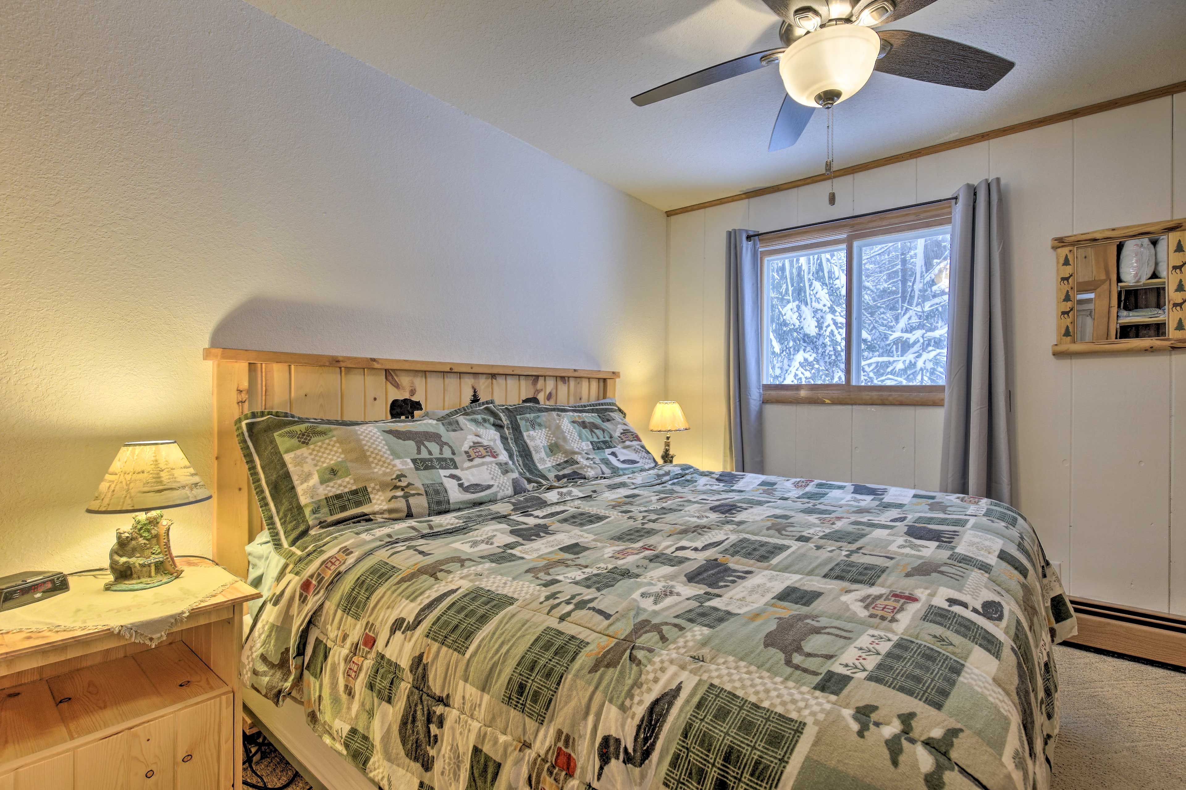 A bedroom with a bed, a nightstand, a lamp, a ceiling fan, and a window with curtains.