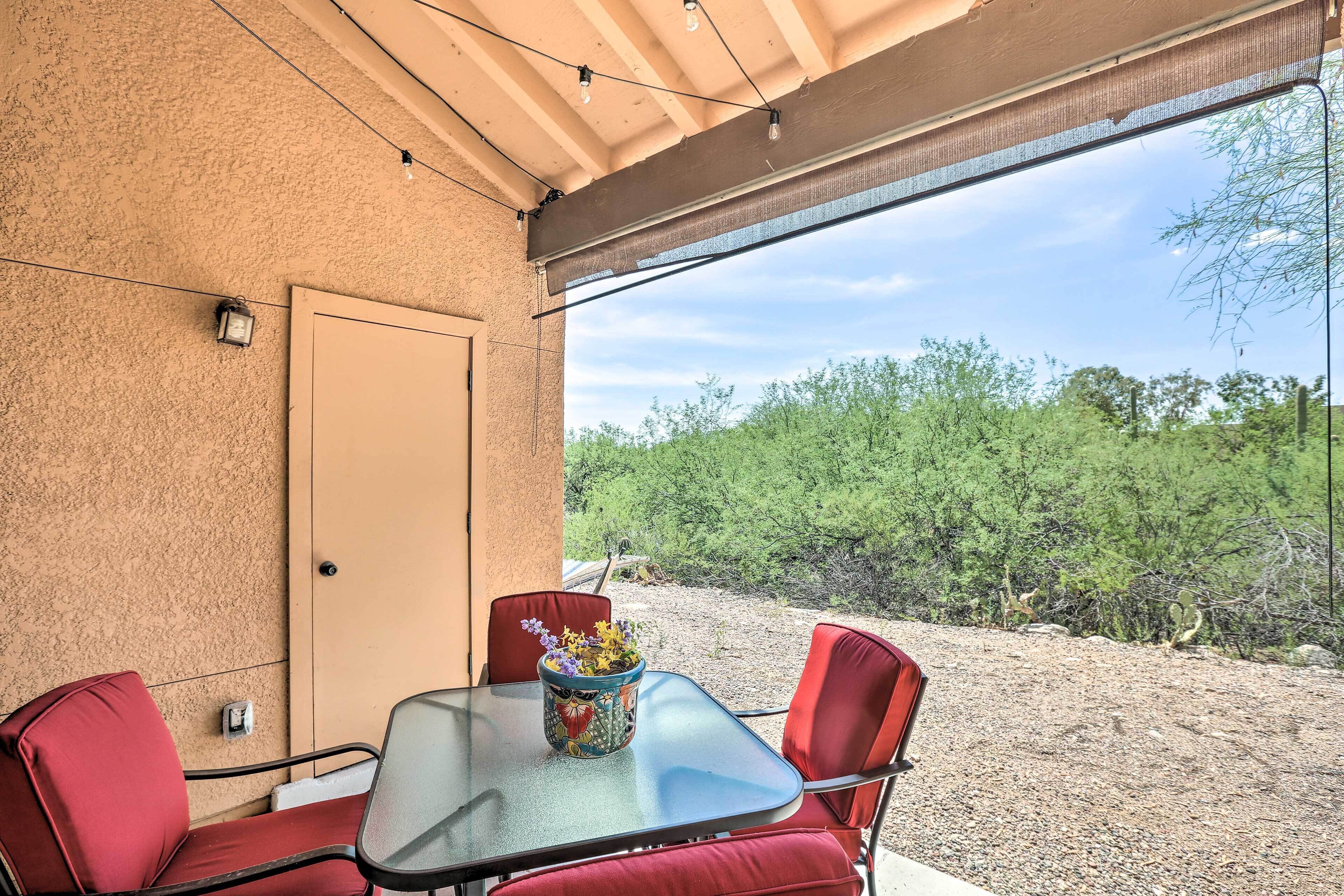 A covered patio with a table and chairs, a potted plant, and a view of a desert landscape.