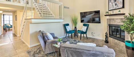 A spacious living room with a staircase, comfortable seating, a fireplace, and a TV mounted on the wall.