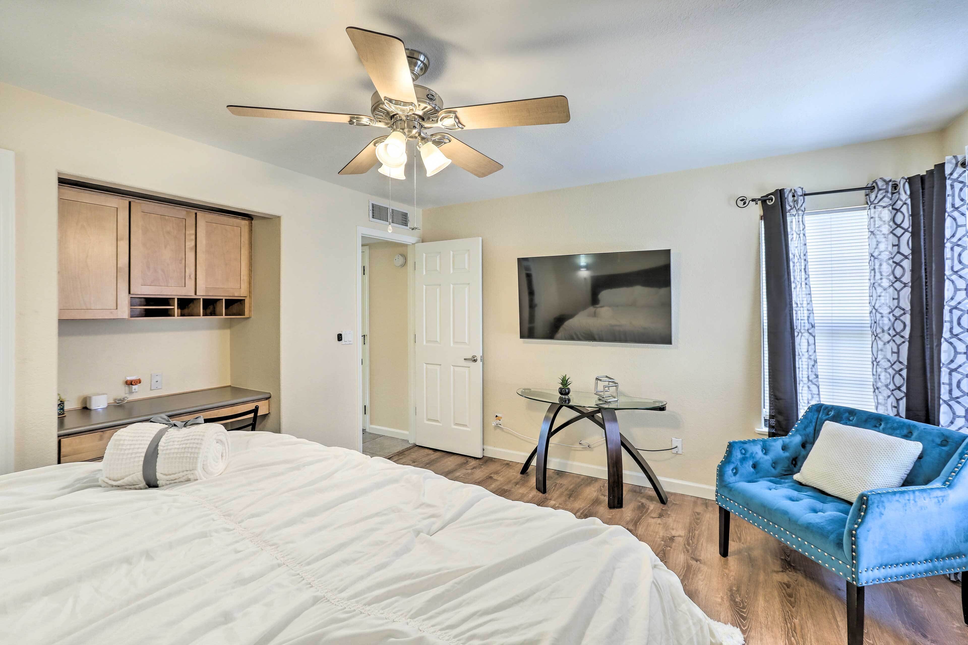 Une chambre à coucher comprenant un lit, un ventilateur de plafond, un bureau, une chaise et un téléviseur.