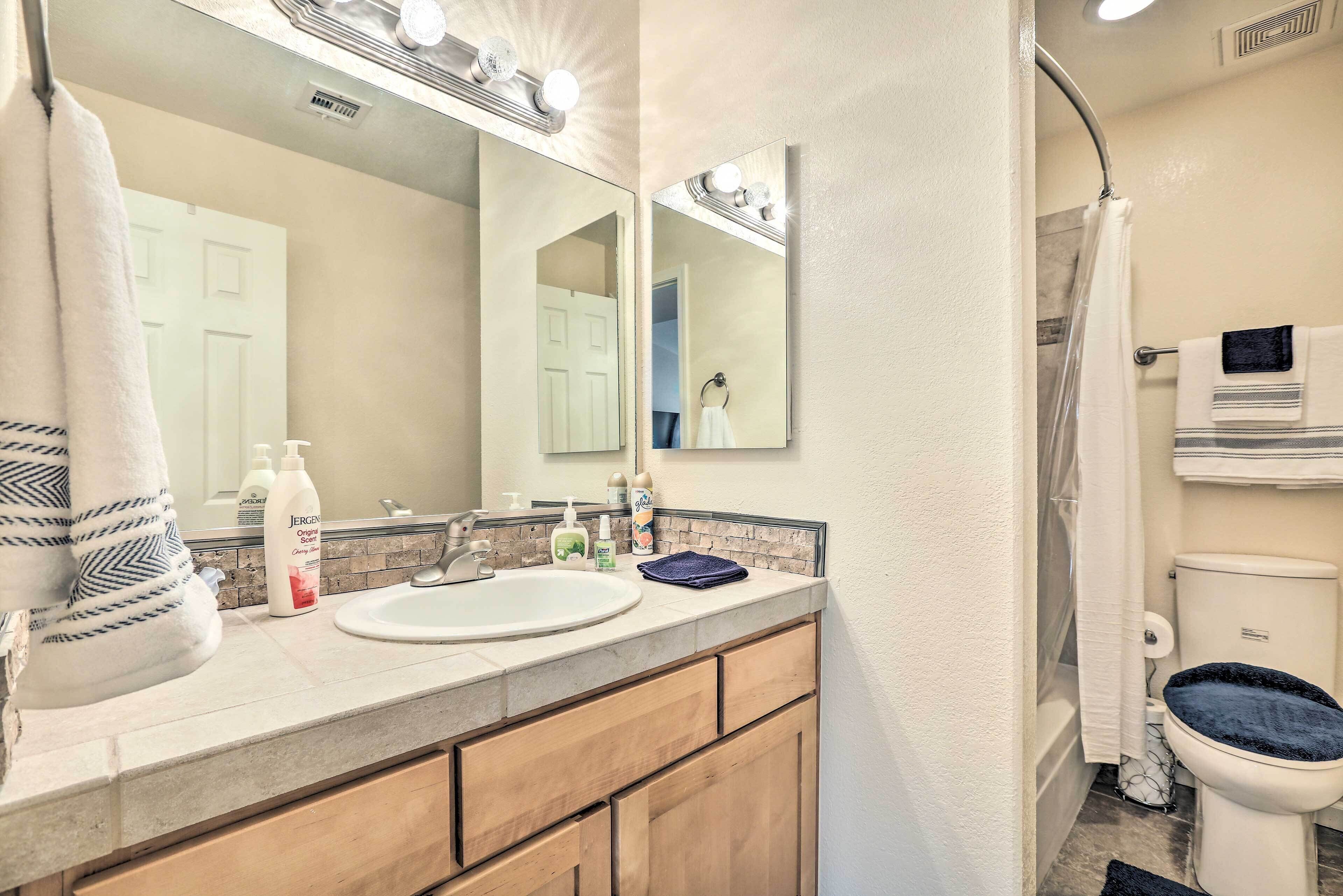 A bathroom with a sink, mirror, and toilet. There are towels and toiletries on the counter.