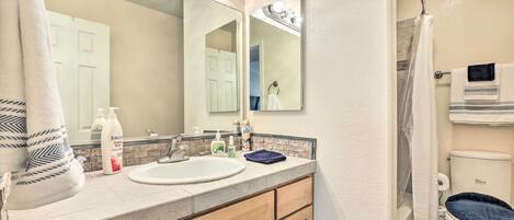 A bathroom with a sink, mirror, and toilet. There are towels and toiletries on the counter.