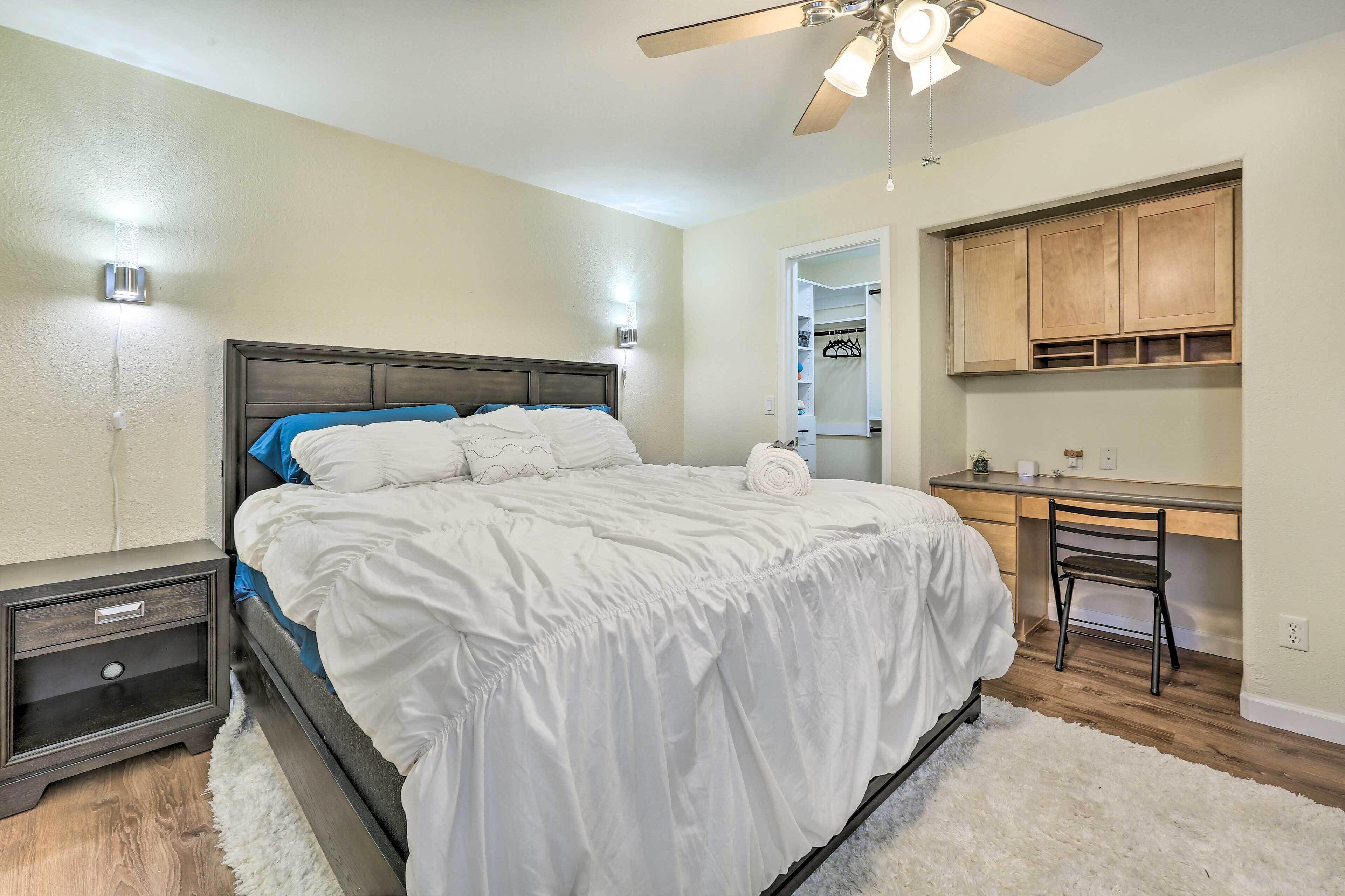 A bedroom with a bed, bedside tables, a desk, and a ceiling fan.