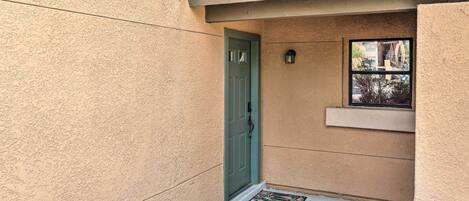 A beige exterior wall with a green door and a small window.