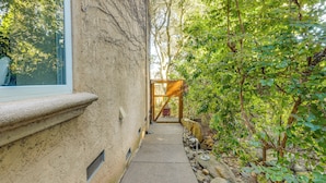 A narrow concrete pathway flanked by a textured wall and dense foliage, leading to a wooden gate. - Santa Rosa Home w/ Private Pool & Tennis Court (Santa Rosa)