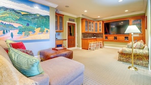 A living room with a large painting, a sofa, a coffee table, and a TV in a kitchen area with wooden cabinets and a bar stool. - Santa Rosa Home w/ Private Pool & Tennis Court (Santa Rosa)