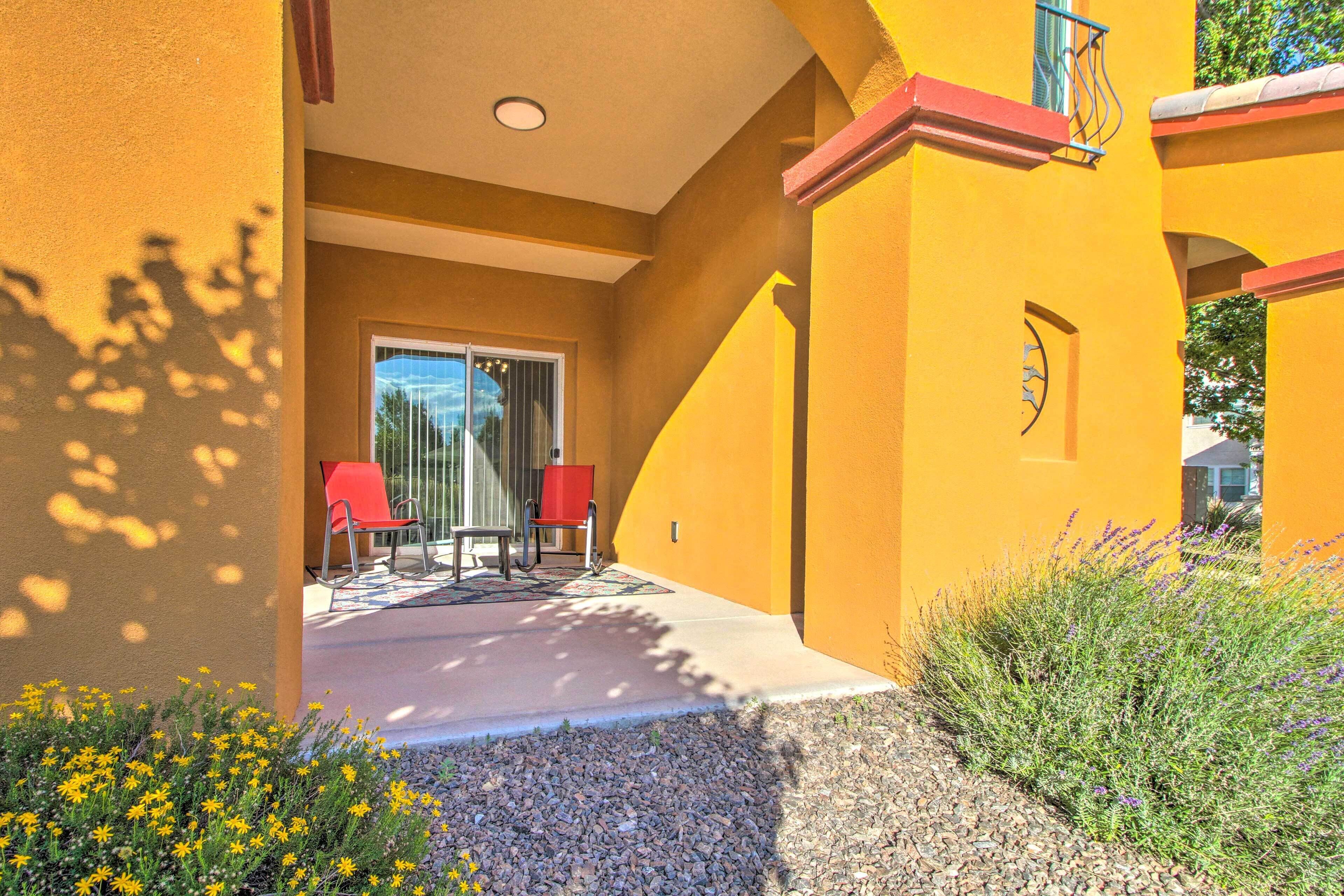 A yellow building with a covered patio, red chairs, and a small garden with yellow flowers.