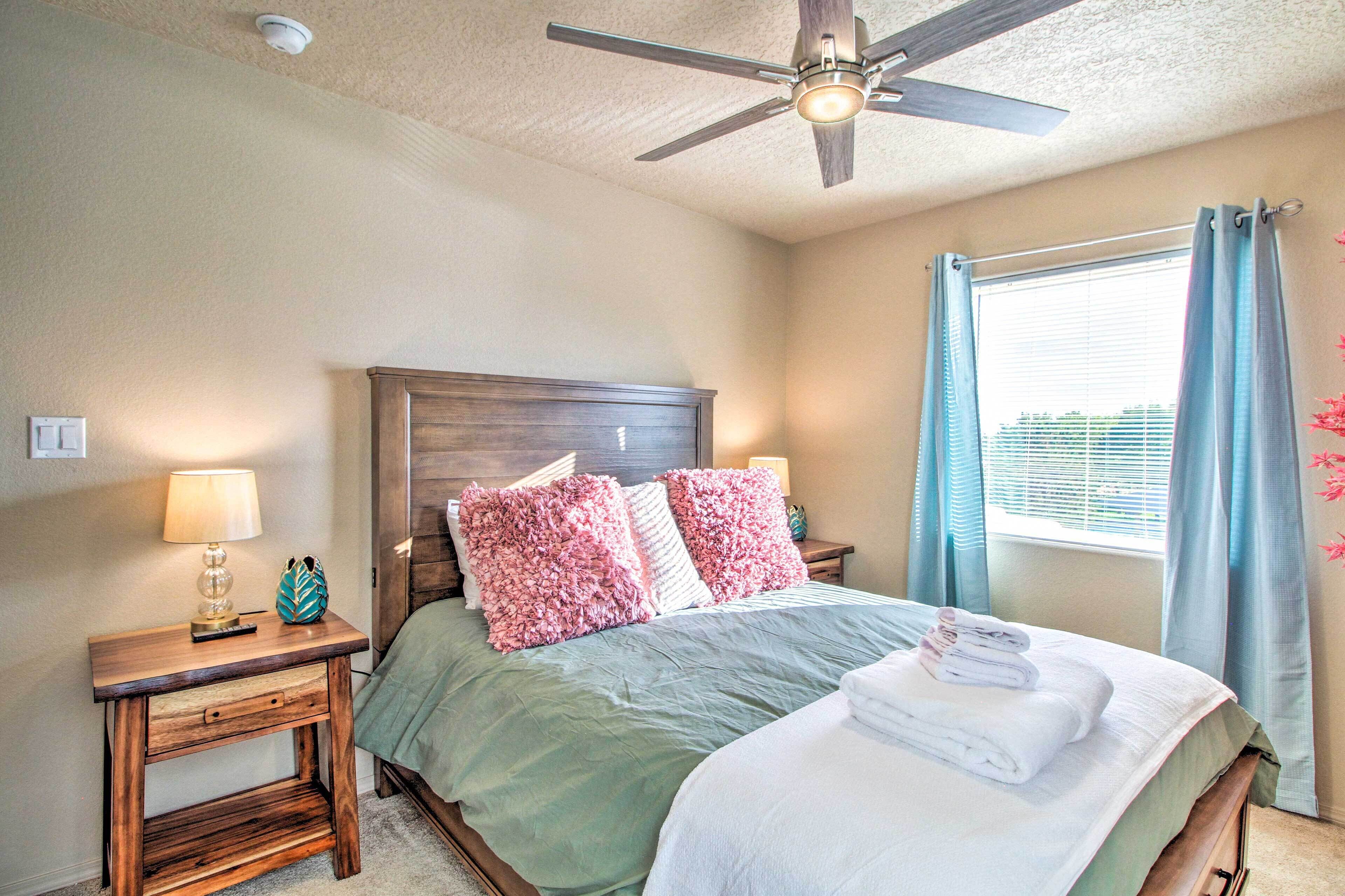 A bedroom with a bed, a nightstand, a ceiling fan, and a window with curtains.