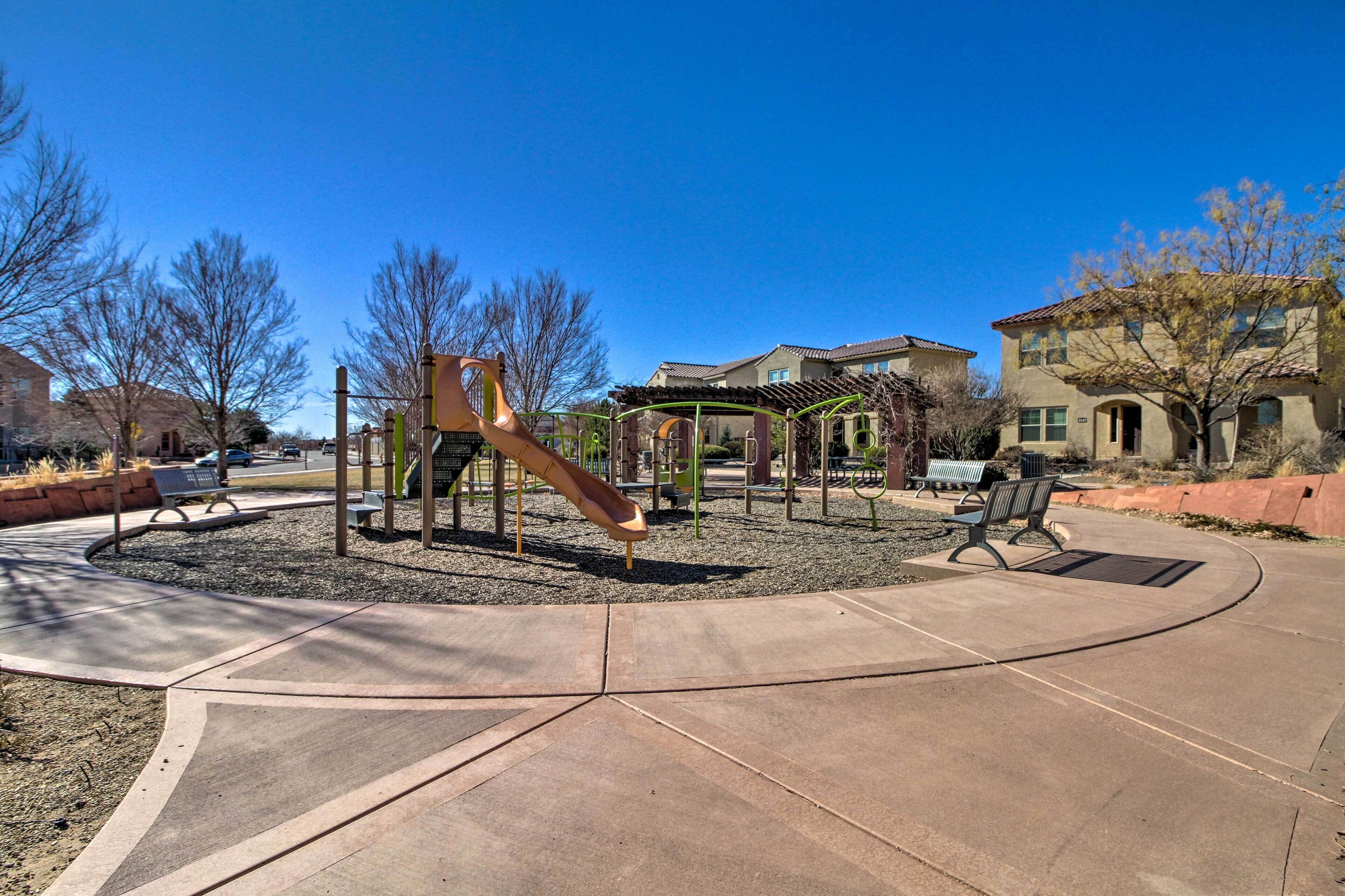 A playground with a slide and swings, surrounded by a paved area with benches.