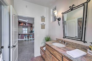Une salle de bain avec un meuble-lavabo en marbre, un grand miroir et un évier. Il y a deux appliques murales et une plante en pot.