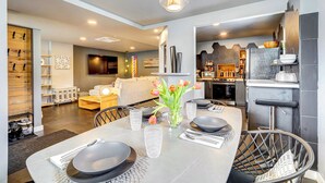 A modern dining area with a table set for four, a vase with flowers, and a kitchen in the background. - 'little House on the Lot' Dryden Townhome: Pets OK (Dryden)