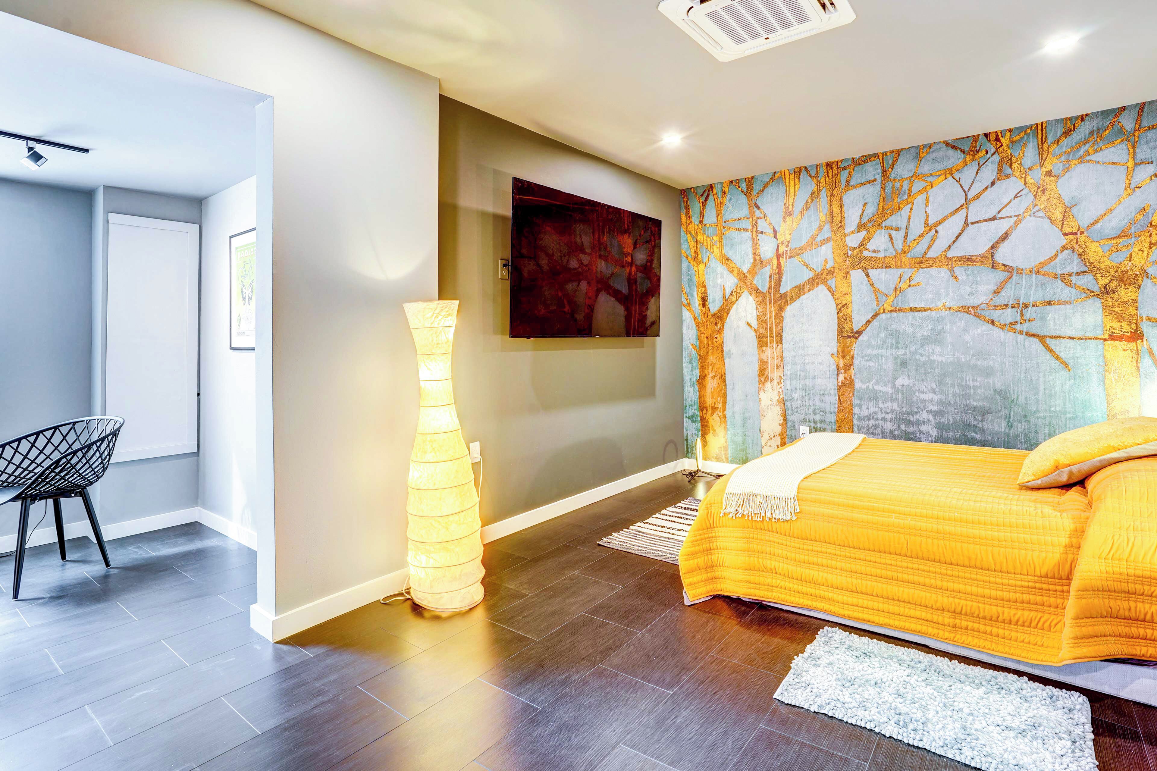 A modern bedroom with a large bed, a wall-mounted TV, a tall floor lamp, and a chair.