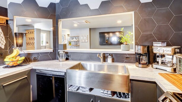 A modern kitchen with a large island, stainless steel appliances, and a hexagonal tile backsplash. - 'little House on the Lot' Dryden Townhome: Pets OK (Dryden)