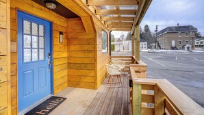 A wooden cabin with a blue door, a porch with rocking chairs, and a view of a street and buildings. - 'little House on the Lot' Dryden Townhome: Pets OK (Dryden)