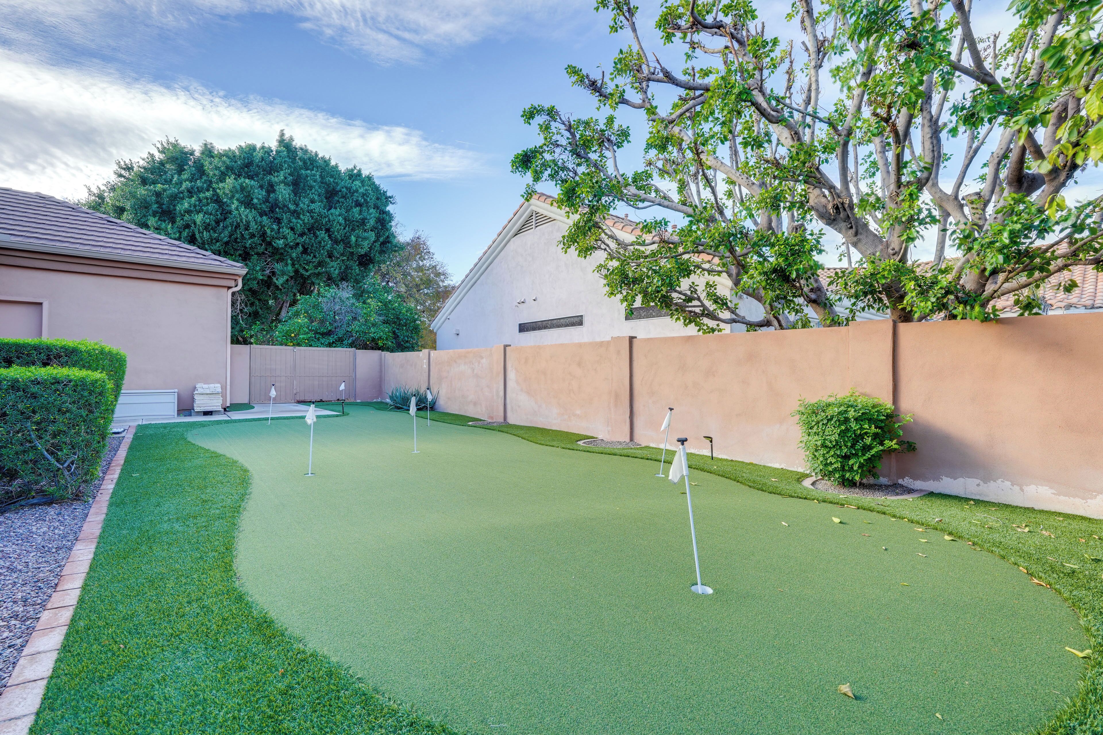 Un campo de mini golf con superficie de césped verde, banderas y una pared color beige al fondo.