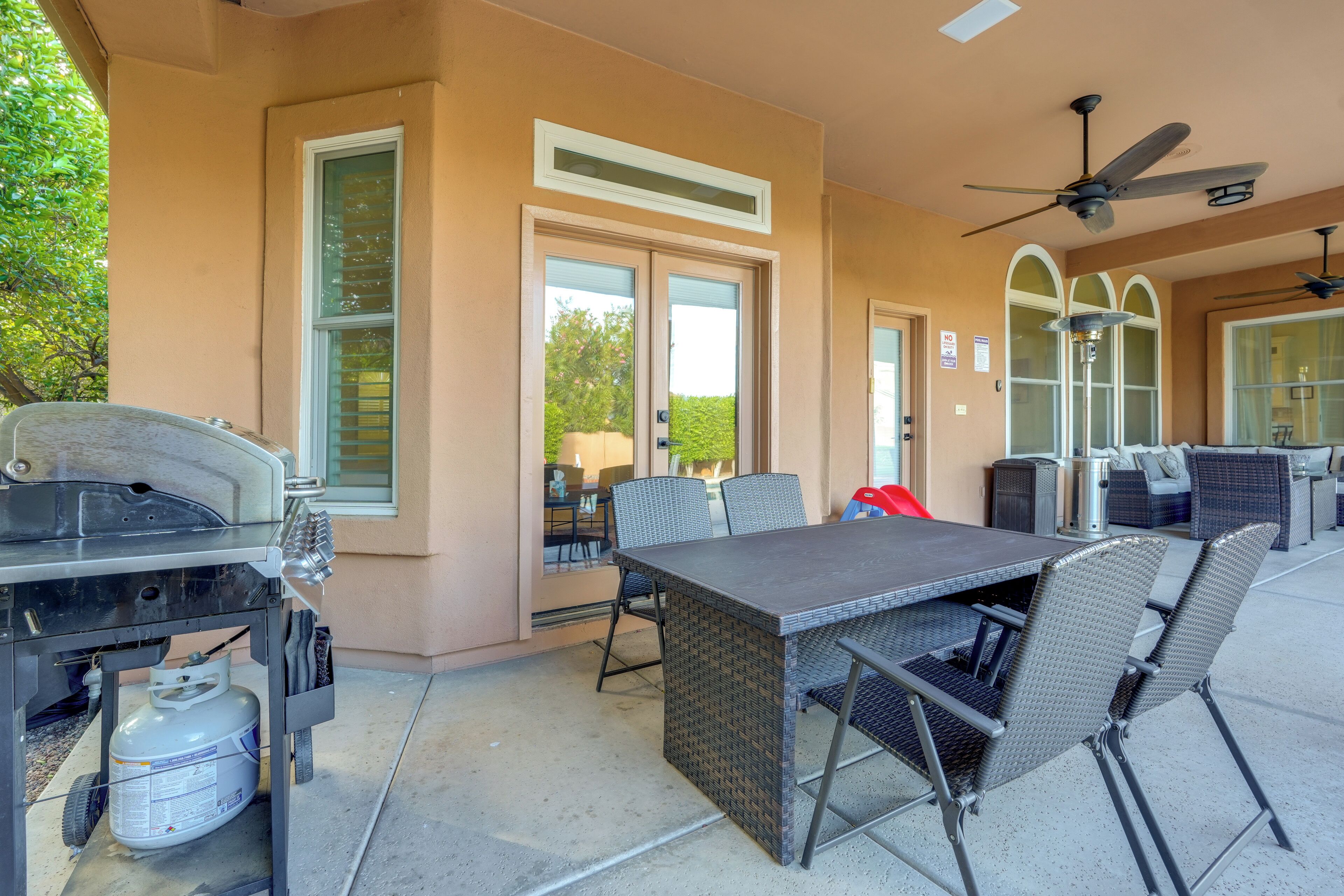 An outdoor patio with a table and chairs, a grill, and a ceiling fan.