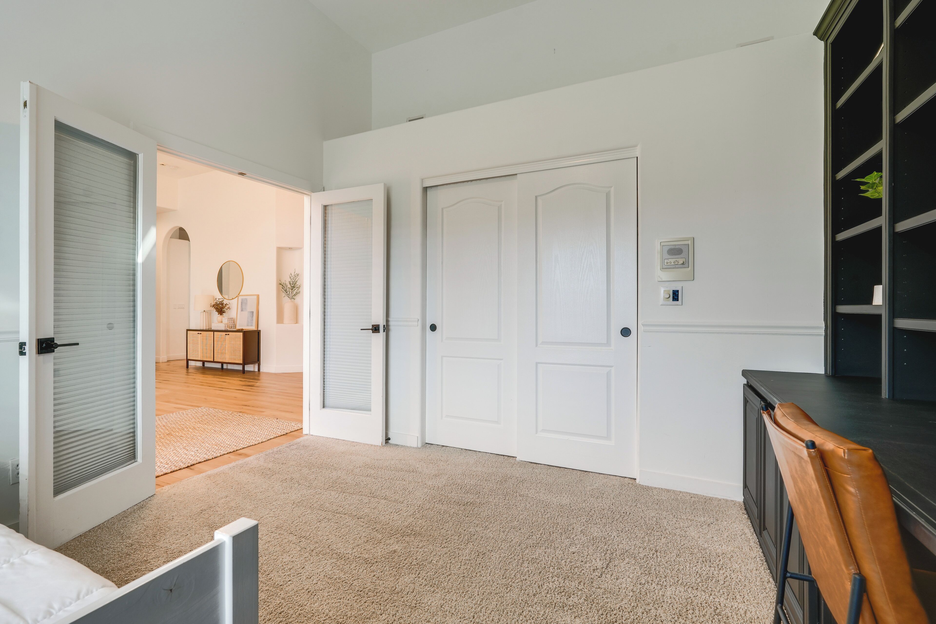 A room with a carpeted floor, white walls, a closed door, a small table with a mirror, and a chair.