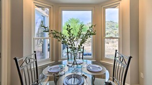 A dining area with a round table set for four, flanked by two chairs, with a view of a desert landscape through large windows. - Gold Canyon Getaway w/ Golf + Community Perks (Gold Canyon)