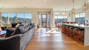 A spacious living room with a large sofa and a kitchen area with bar stools. - Prescott Vacation Rental w/ Game Room & Mtn Views! (Prescott)