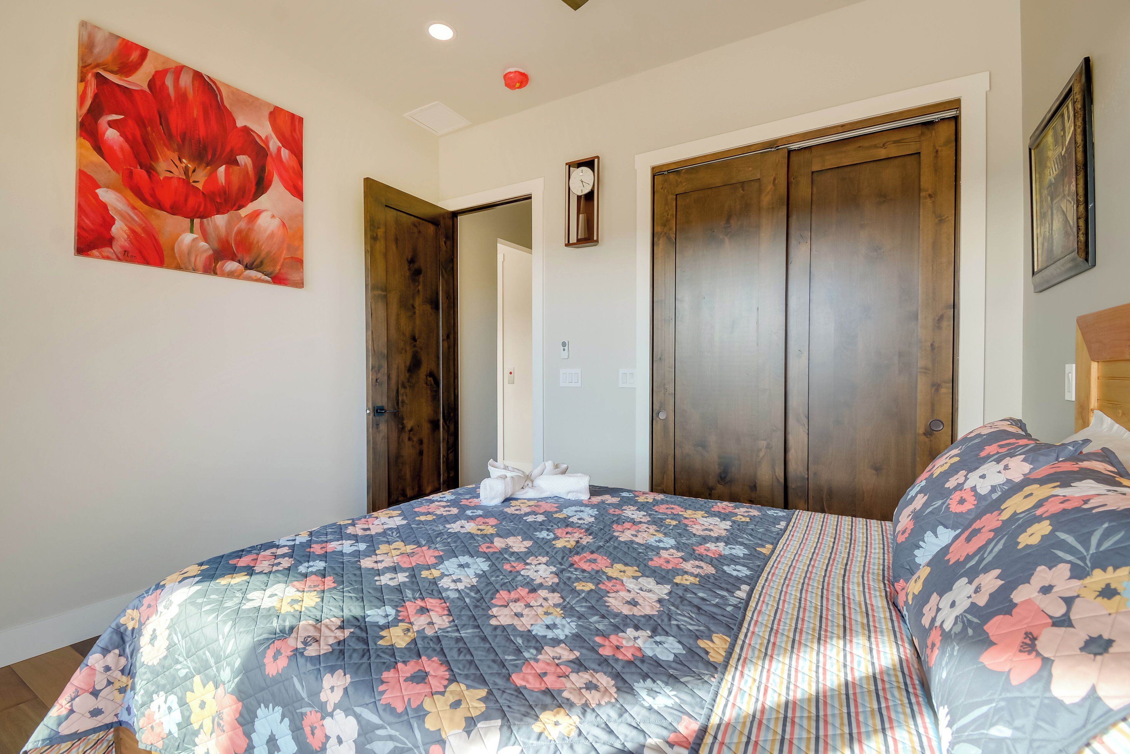 Een slaapkamer met een bloemenbedovertrek, een klok aan de muur en houten deuren.